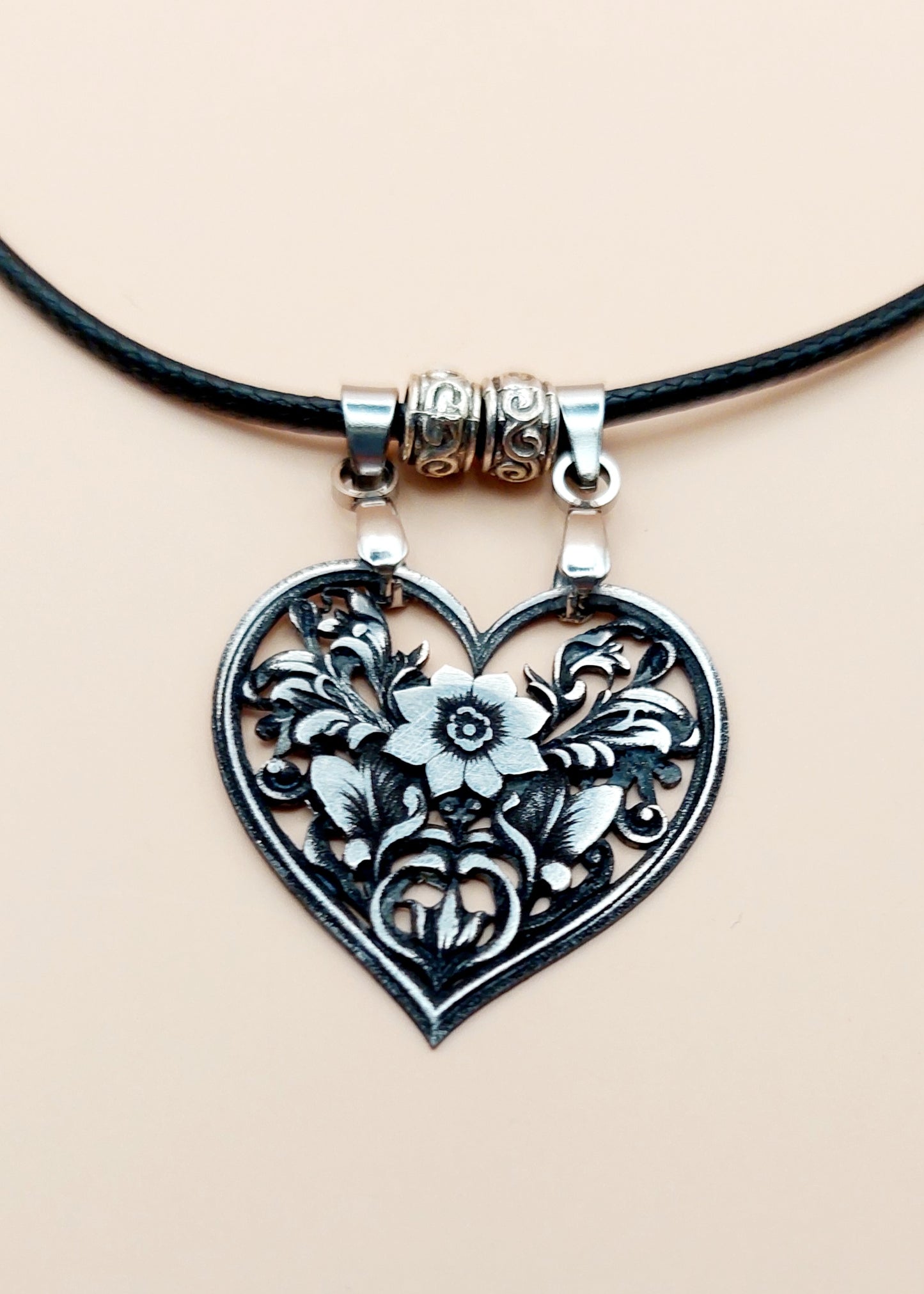 Heart-shaped floral pendant on a black cord against a beige background
