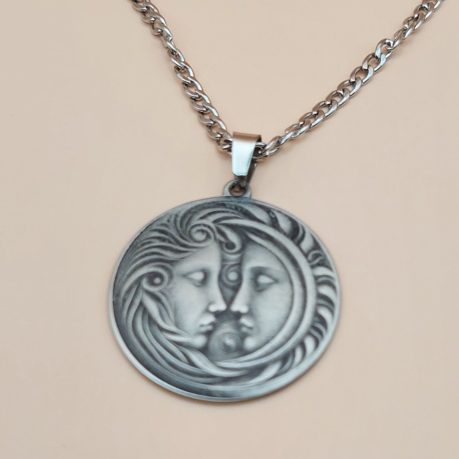 Silver necklace with a round pendant featuring faces on a beige background