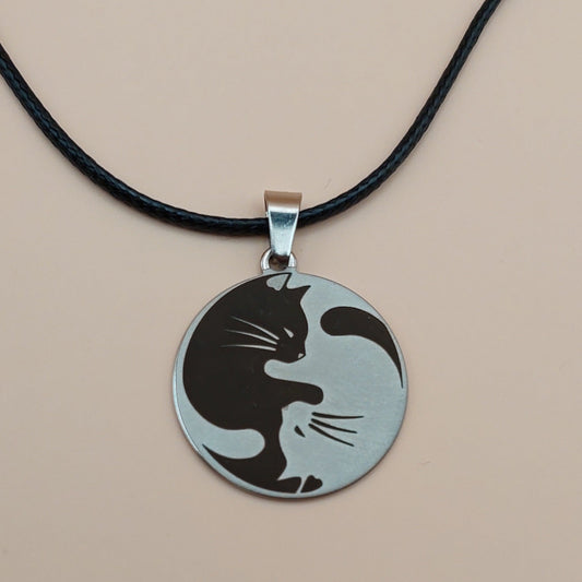 Yin yang cats pendant on a black cord against a beige background