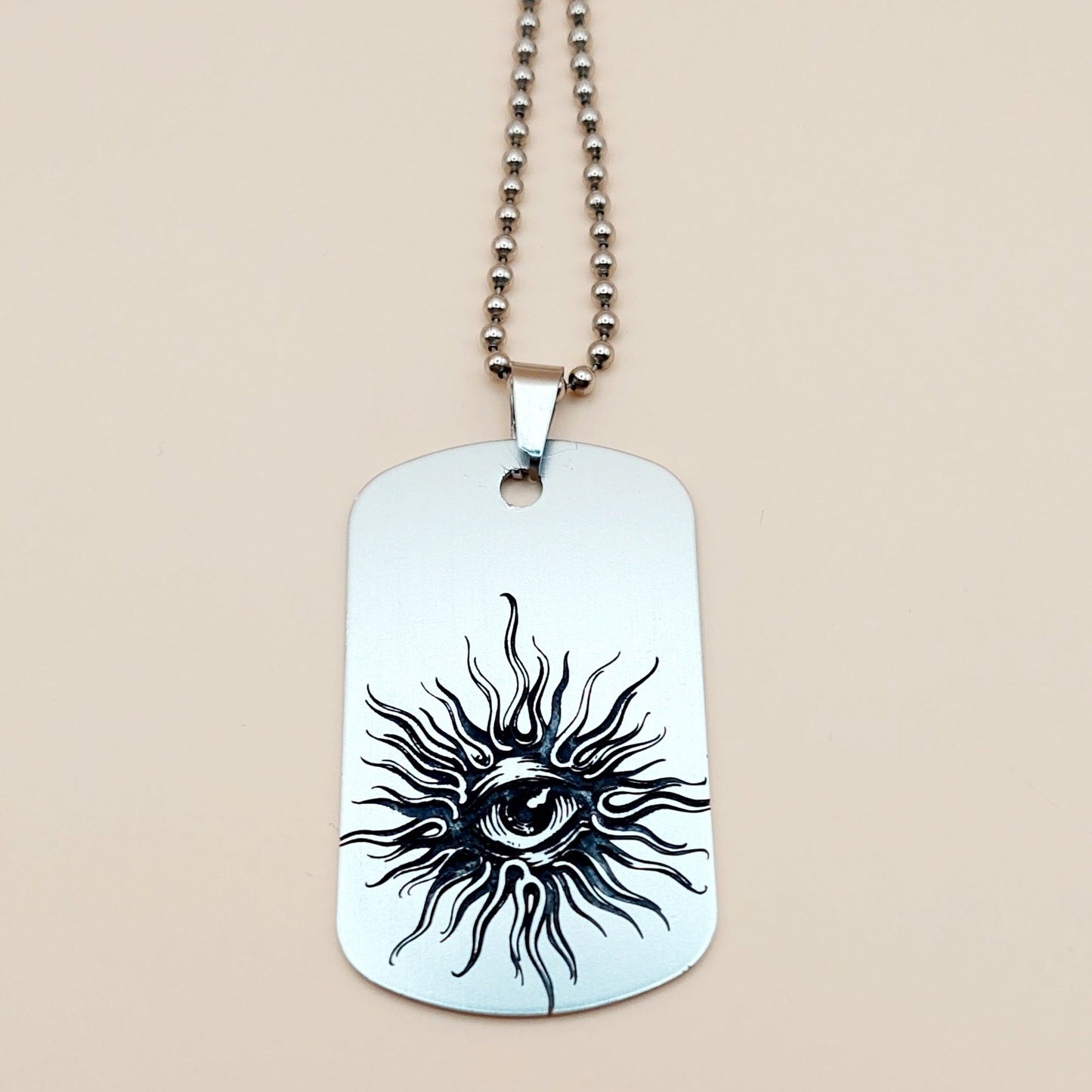 Dog tag necklace with sun and eye design on a beige background