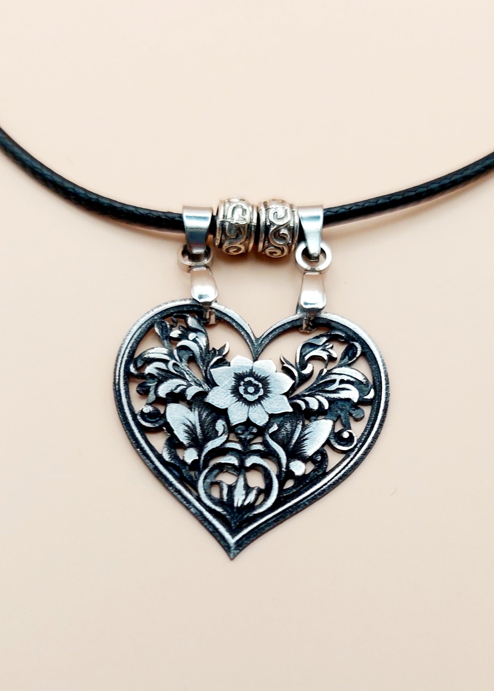 Heart-shaped floral pendant on a black cord against a beige background