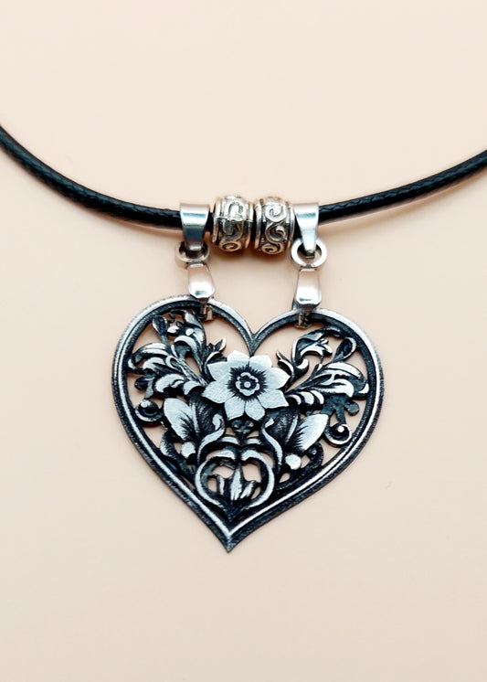 Heart-shaped floral pendant on a black cord against a beige background