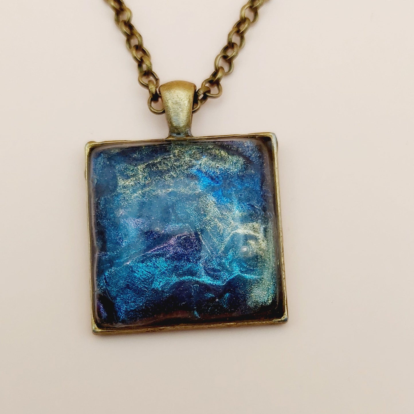 Necklace with a square pendant featuring a blue and white abstract design on a beige background