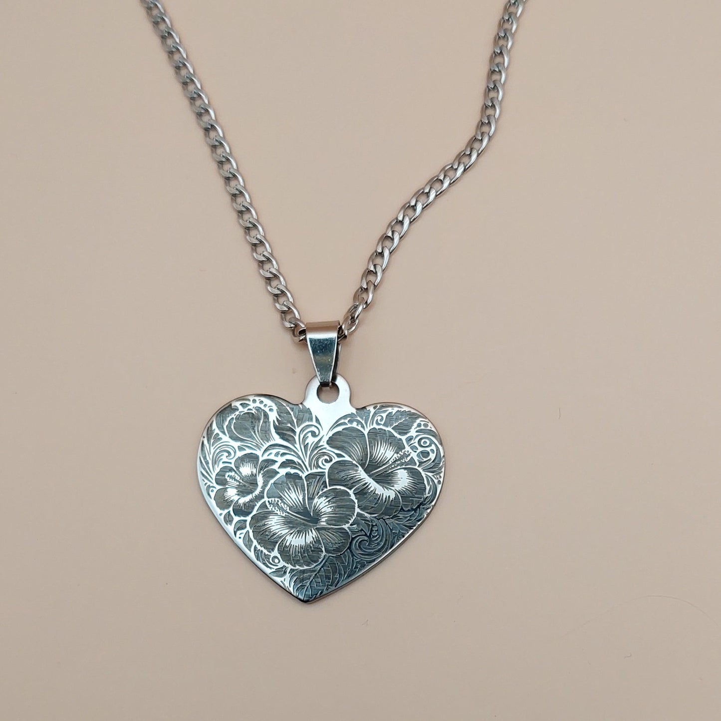 Silver heart-shaped pendant with floral design on a beige background