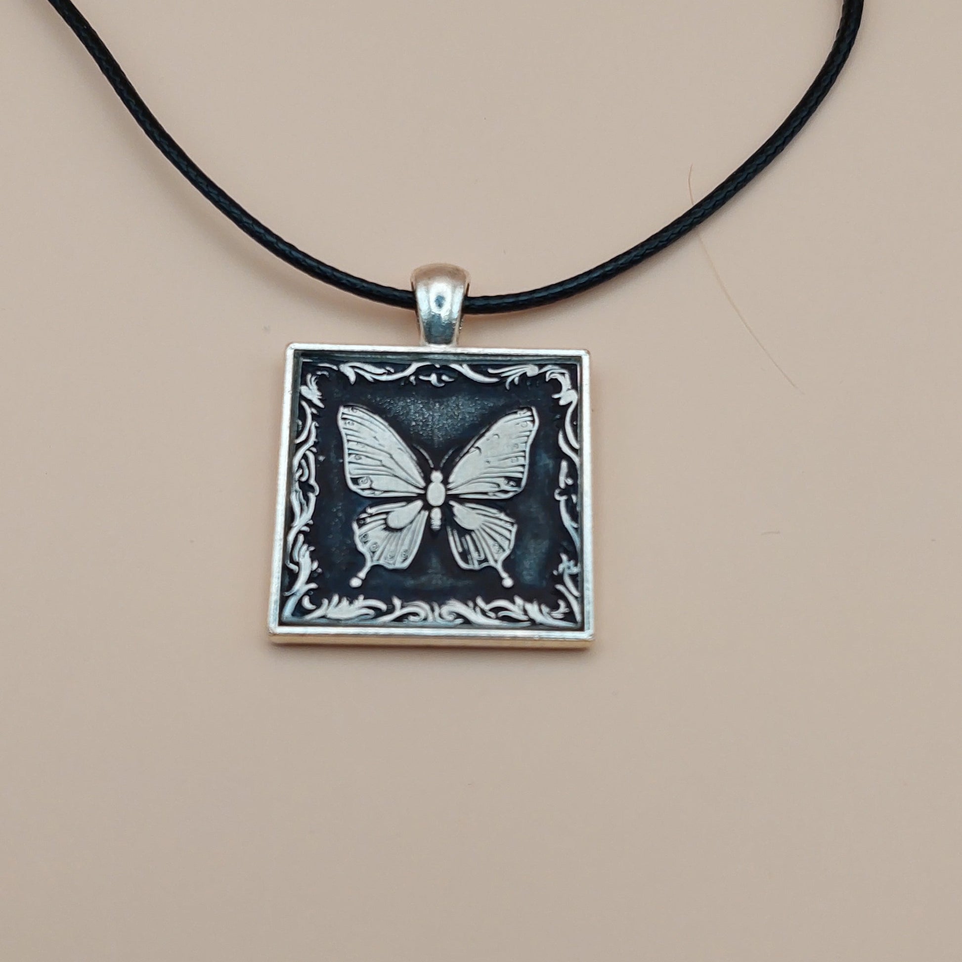 Necklace with a square pendant featuring a butterfly design on a beige background