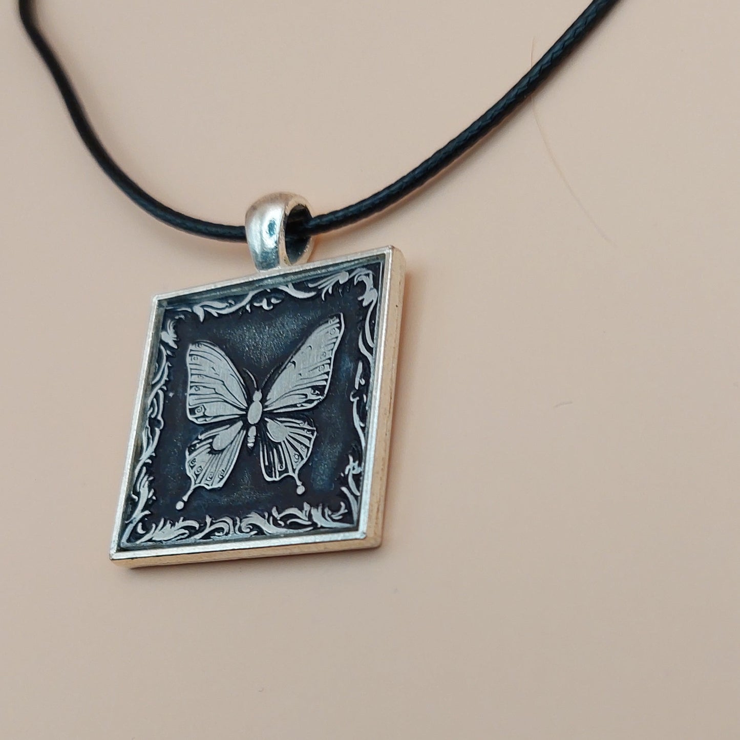 Necklace with a square pendant featuring a butterfly design on a beige background