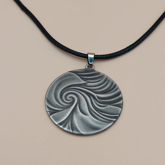 Silver pendant with a spiral design on a black cord against a beige background