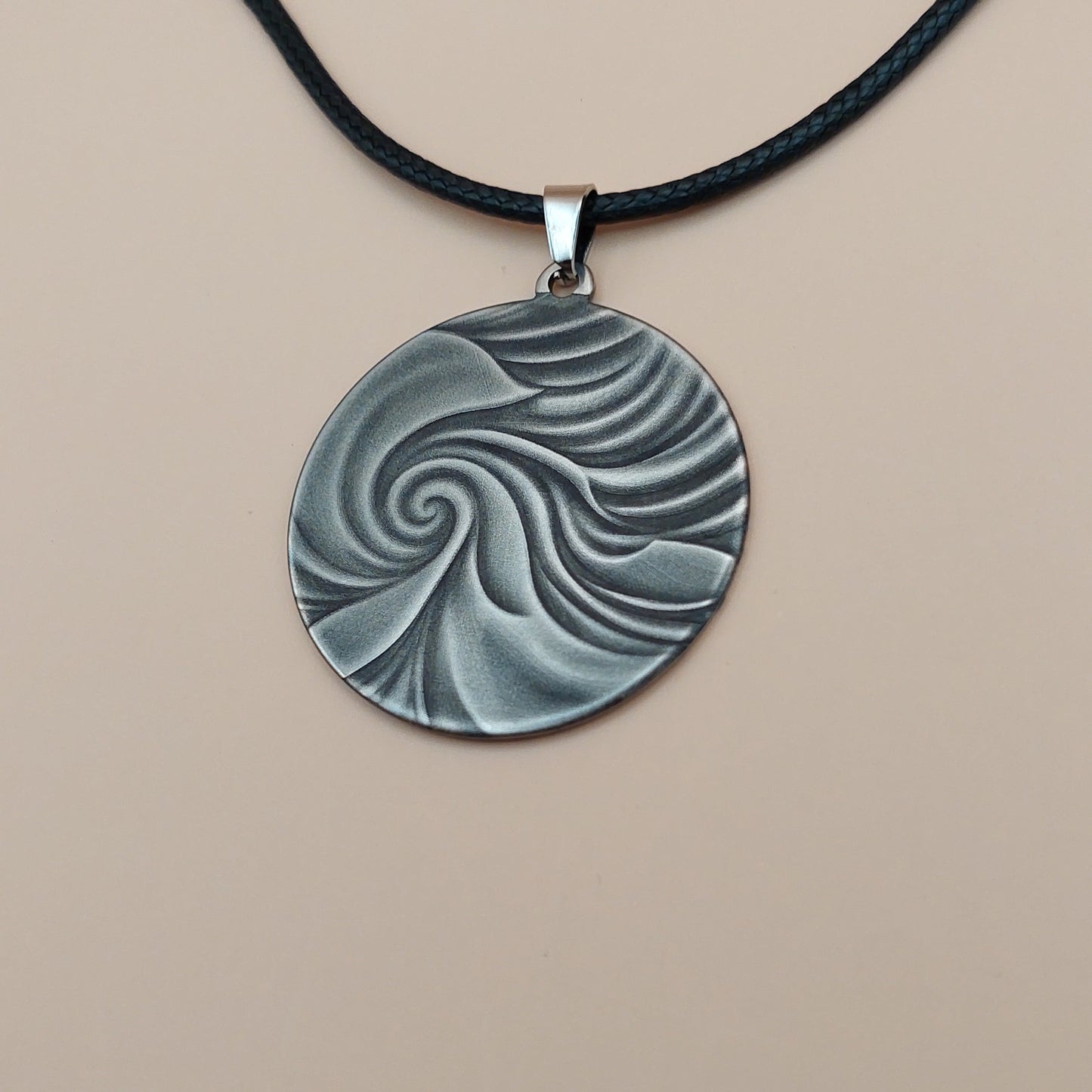 Round pendant with wavy design on a black cord against a beige background