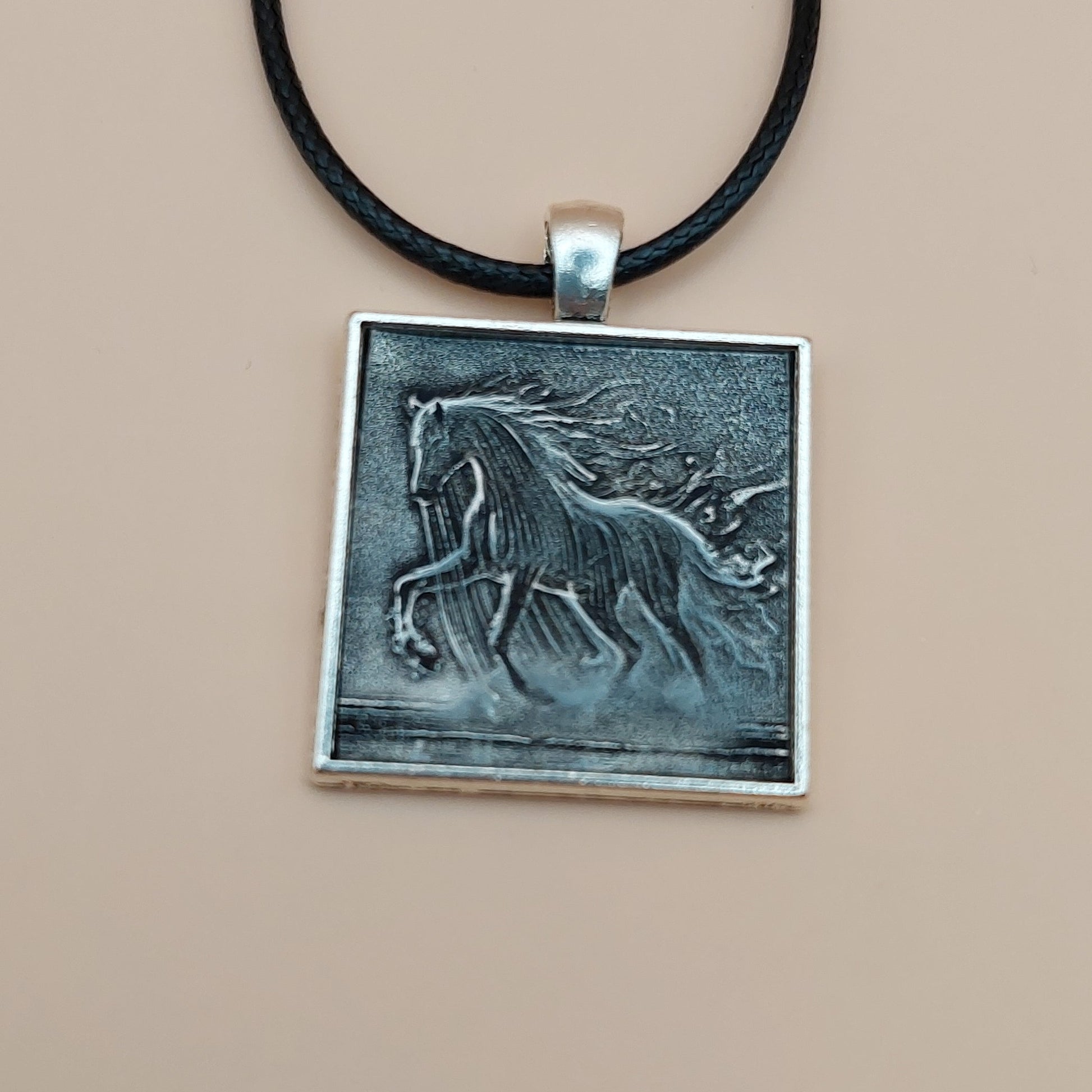 Silver pendant with a black cord on a beige background