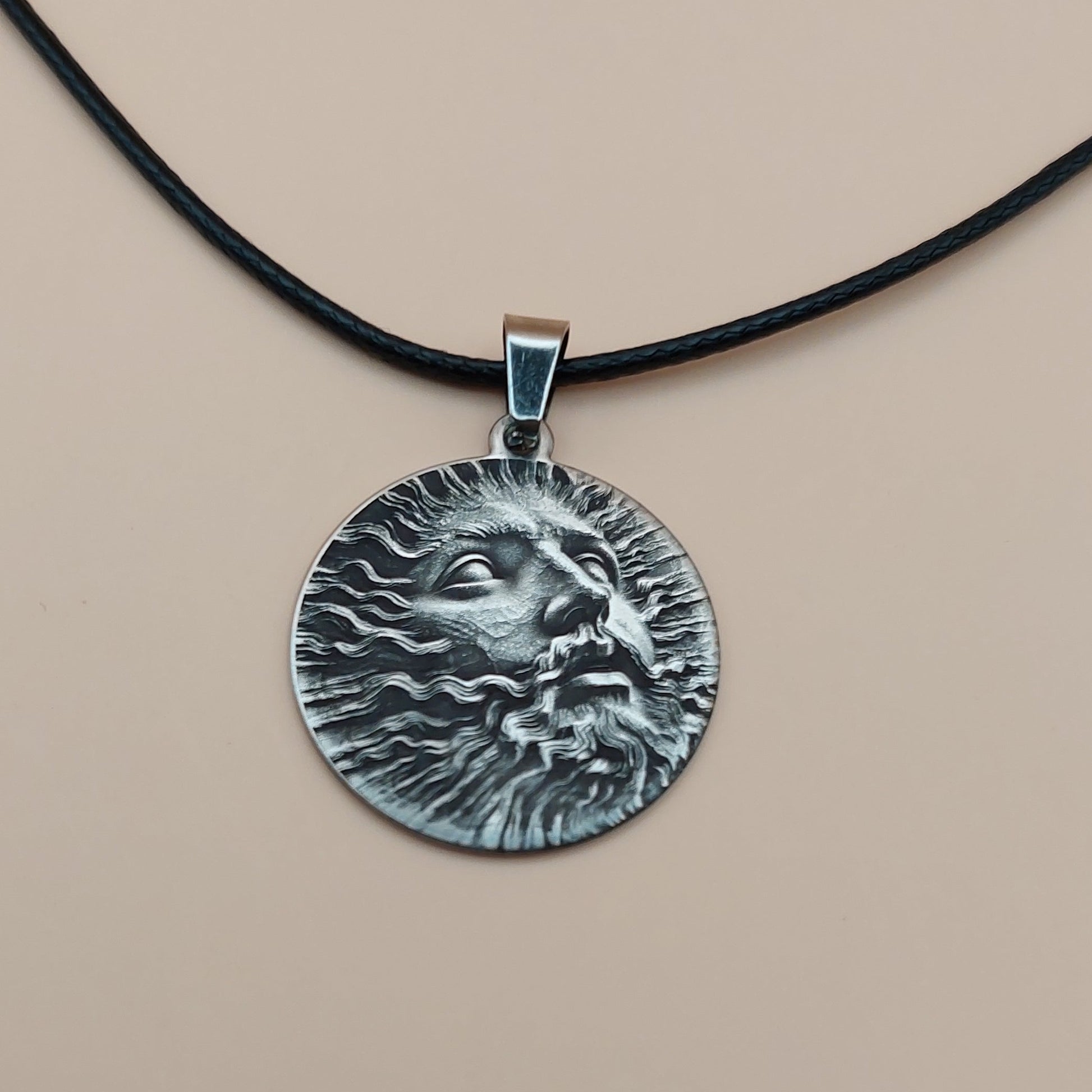 Silver pendant on a black cord against a beige background