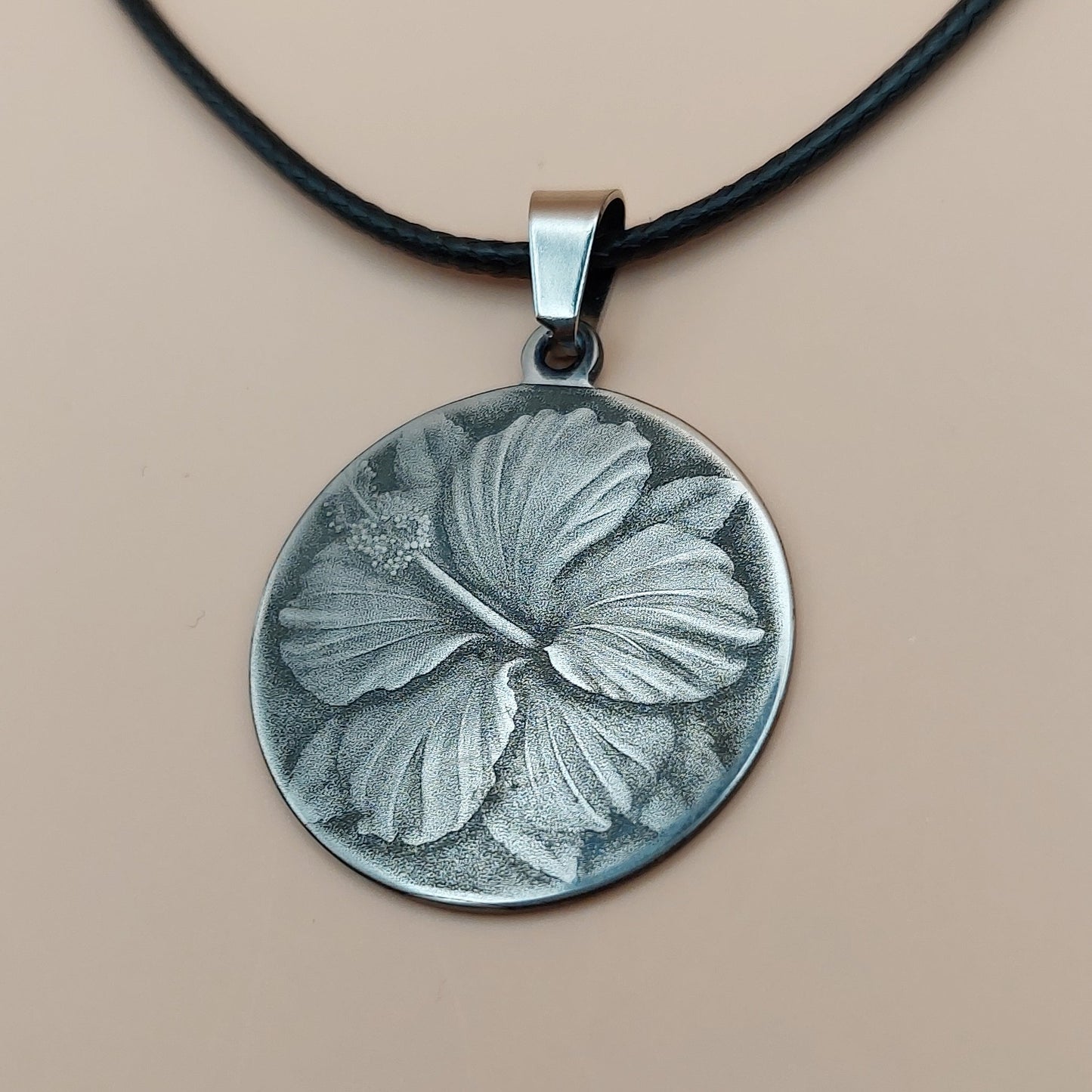 Silver pendant with leaf design on a black cord against a beige background