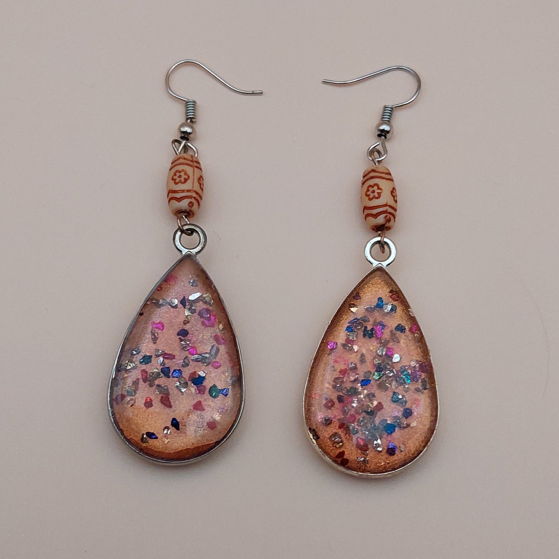 Teardrop-shaped earrings with floral design on a beige background