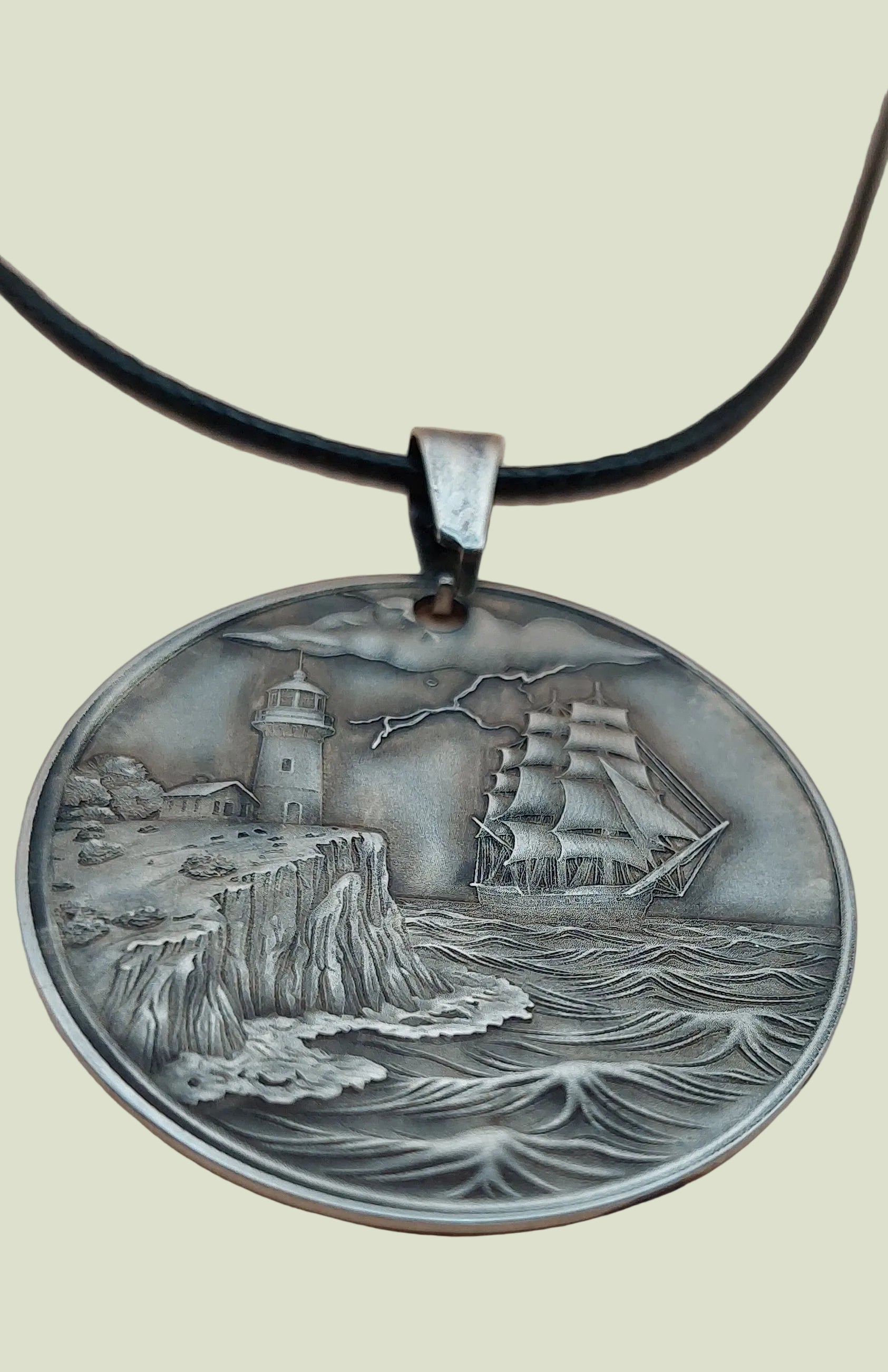 Silver pendant with a lighthouse and ship design on a beige background