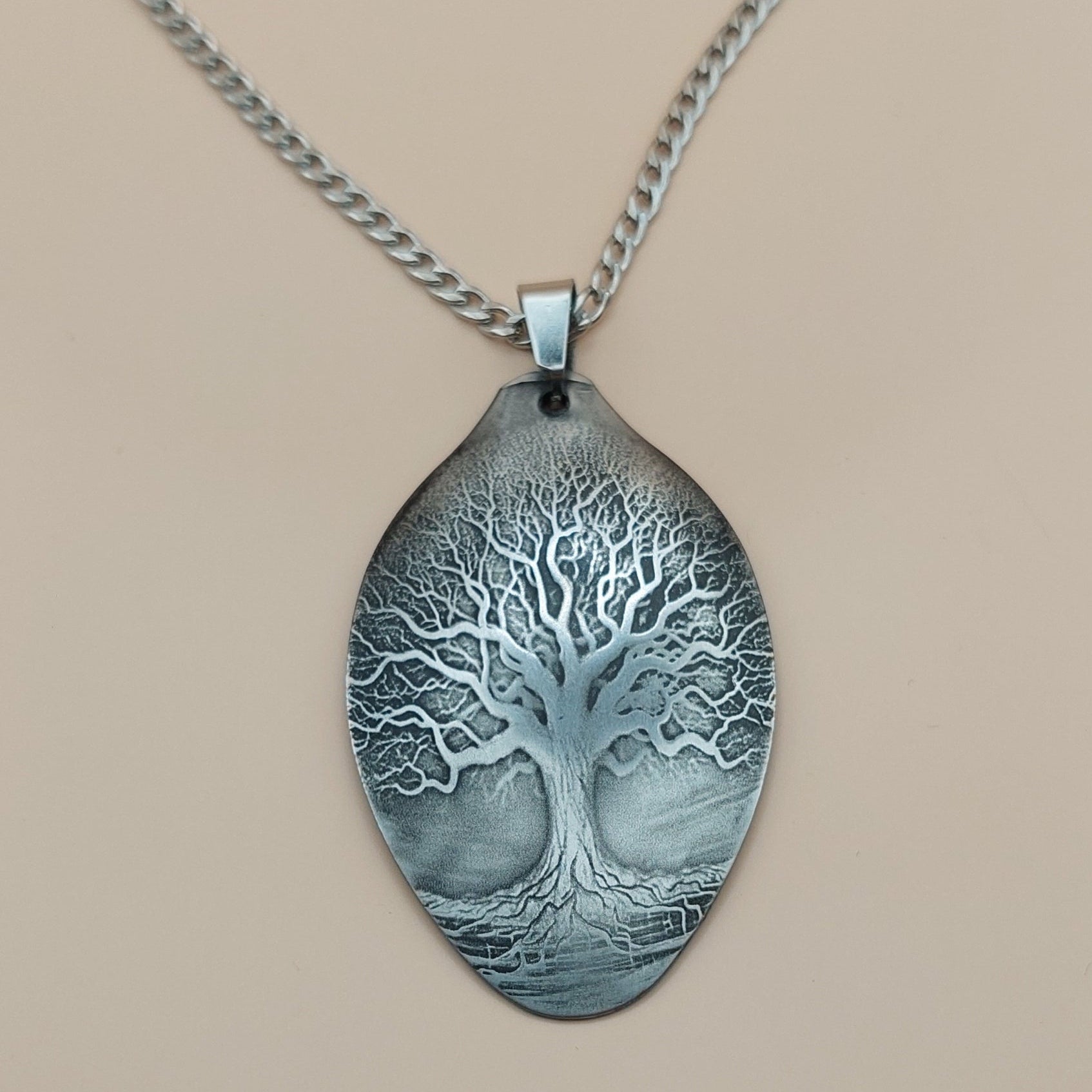 Silver necklace with a tree pendant on a beige background