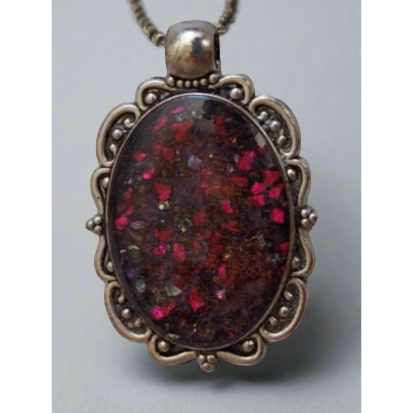 An oval-shaped pendant with a multicolored resin design, encapsulated in a metal frame with intricate details, attached to a silver chain.