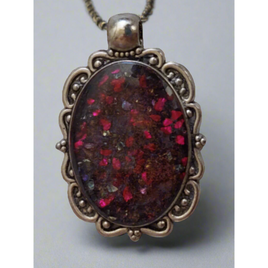 An oval-shaped pendant with a multicolored resin design, encapsulated in a metal frame with intricate details, attached to a silver chain.